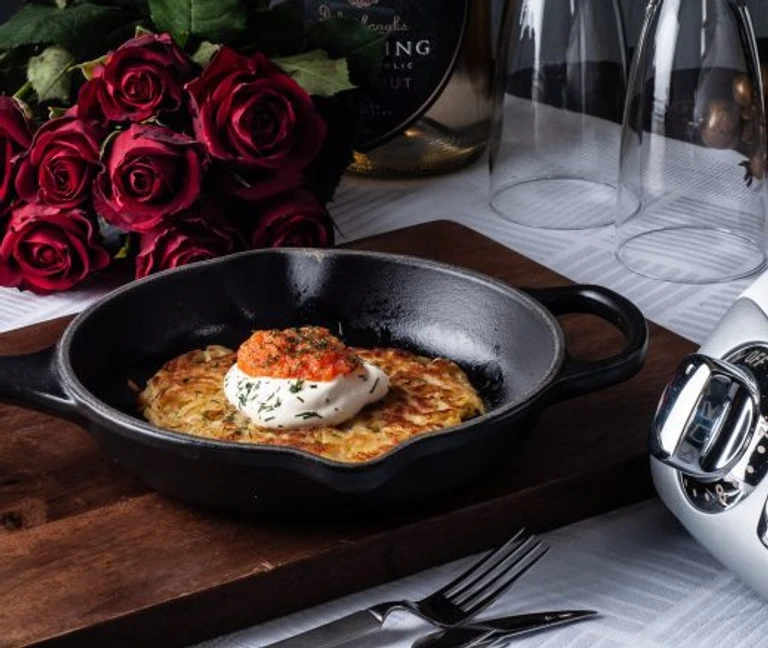Crispy potato rösti in cast iron skillet with sour cream and tomato salsa, made with Ankarsrum stand mixer, beside red roses.
