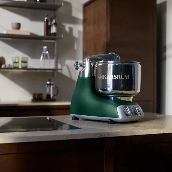 Ankarsrum Assistent Original in Forest Green on a marble kitchen countertop in a dark kitchen.