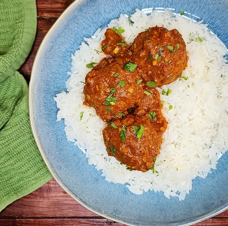 Spiced meatballs in rich tomato curry sauce over fluffy white rice, garnished with fresh cilantro, served in a blue bowl.