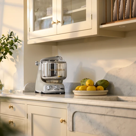 Ankarsrum Assistent Original in Harmony Beige in a bright kitchen, with a bowl of lemons and an artichoke beside it.