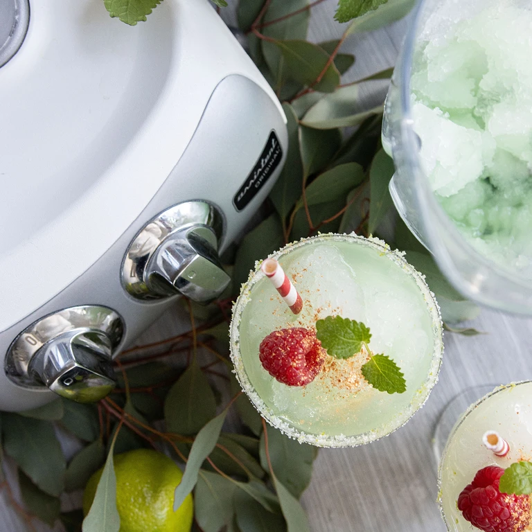 Ankarsrum stand mixer beside frozen margarita cocktails garnished with raspberries, mint leaves, and salted rims.