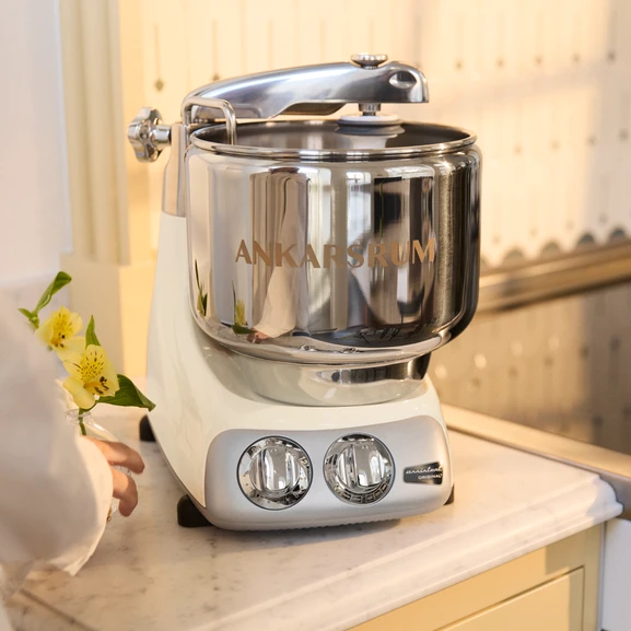 Ankarsrum Assistent Original in der Farbe Creme Light auf einer hellen Küchenarbeitsplatte in einer gelben Küche.