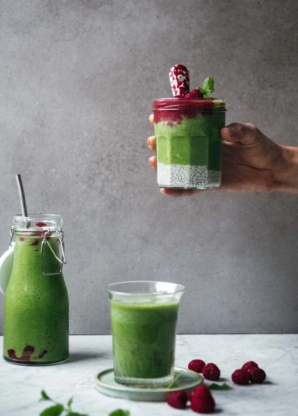 Green smoothie layered with chia pudding and raspberry topping in a jar, with fresh raspberries and mint, by Ankarsrum.