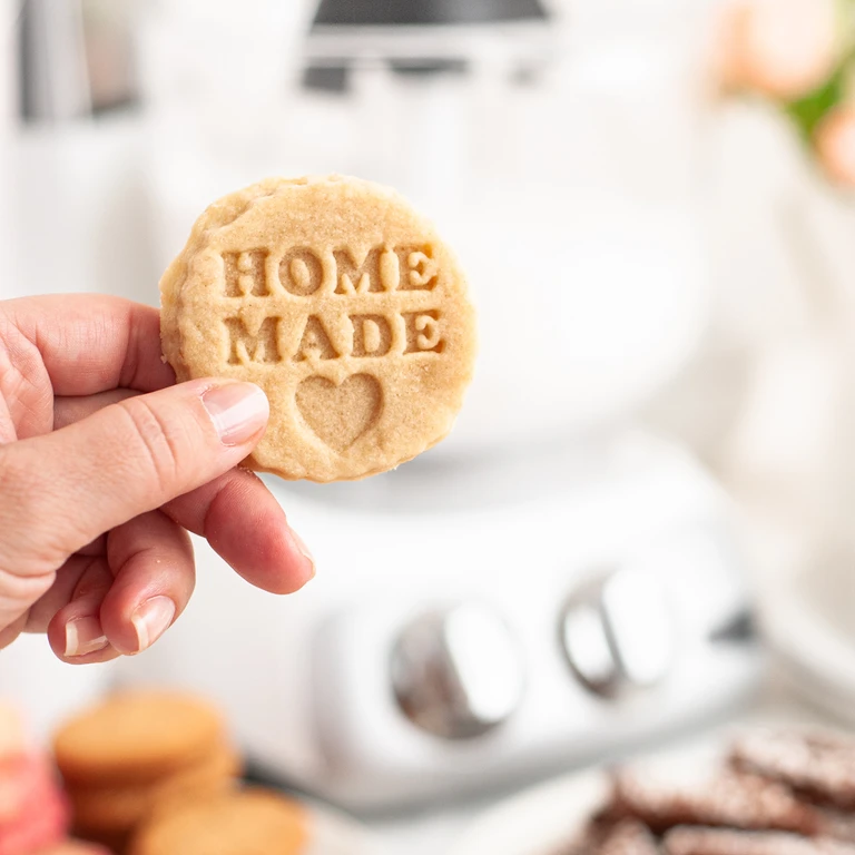 Hand holding a round homemade cookie stamped with HOME MADE and a heart, made with an Ankarsrum stand mixer.