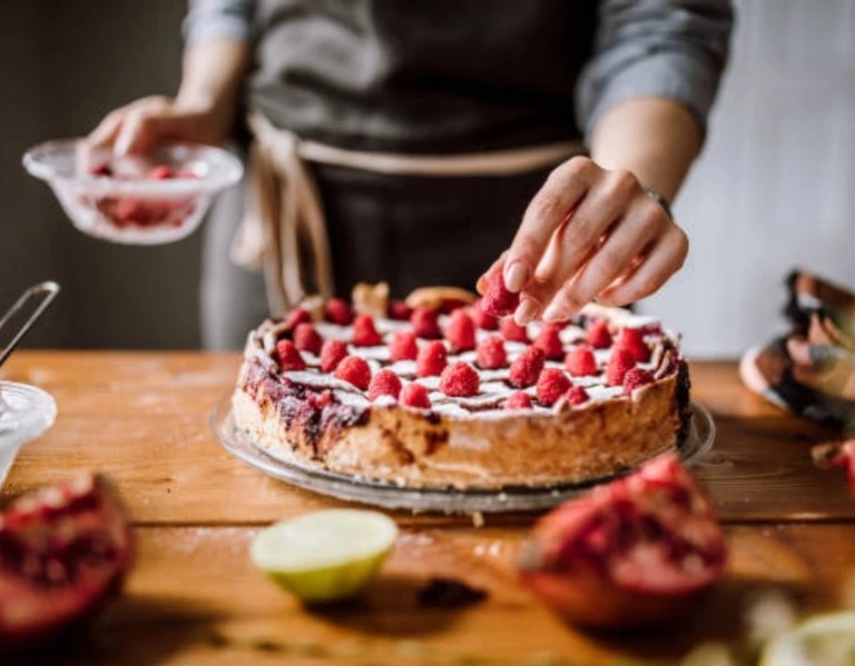 Person decorating a homemade raspberry cheesecake on a wooden table, showcasing baking results with an Ankarsrum stand mixer.