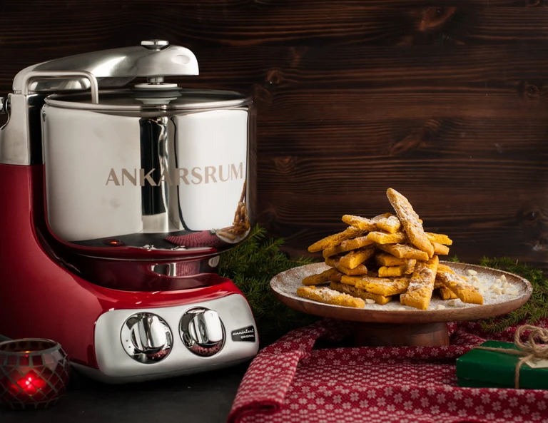 Ankarsrum red stand mixer beside a plate of powdered sugar Christmas cookies on a festive holiday table setting.