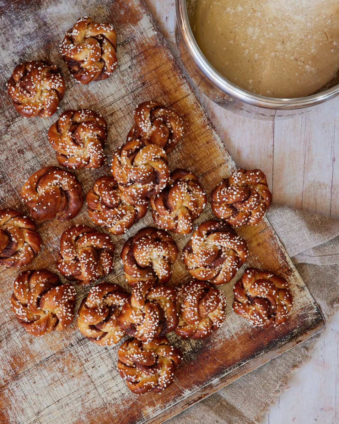 Freshly baked Swedish cardamom knots topped with pearl sugar on a rustic wooden board, made with Ankarsrum stand mixer.