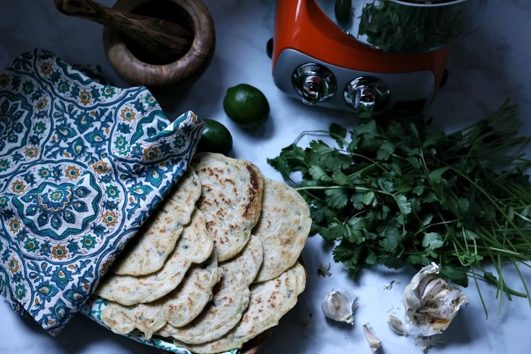 Freshly made herb flatbreads with cilantro, garlic, and lime beside an Ankarsrum stand mixer on marble surface.