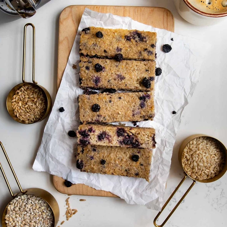 Blueberry oat bars sliced on parchment paper with gold measuring cups of grains, made with Ankarsrum stand mixer.