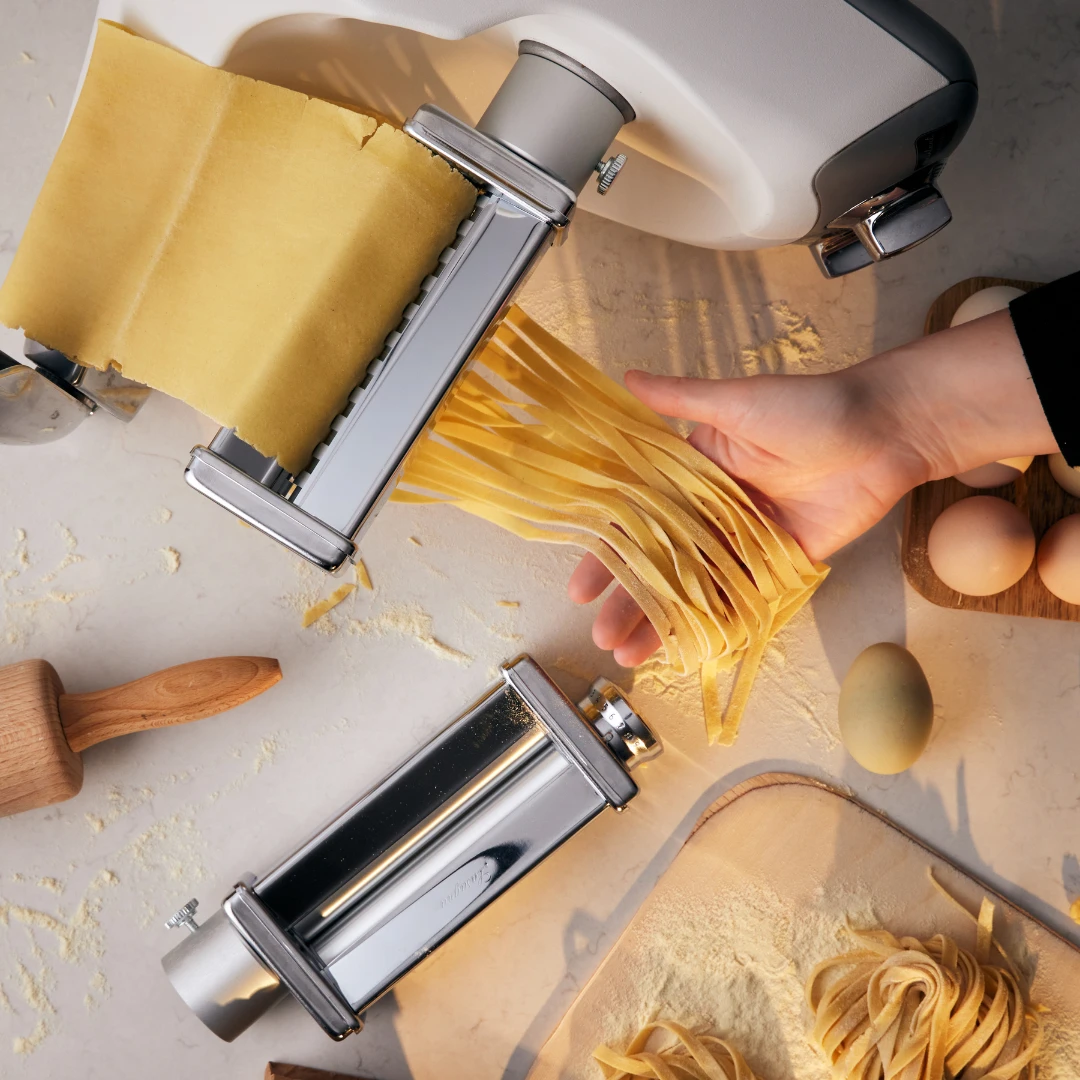 Hand som fångar nygjord fettuccine när degen passerar genom Ankarsrums pastavalsar.