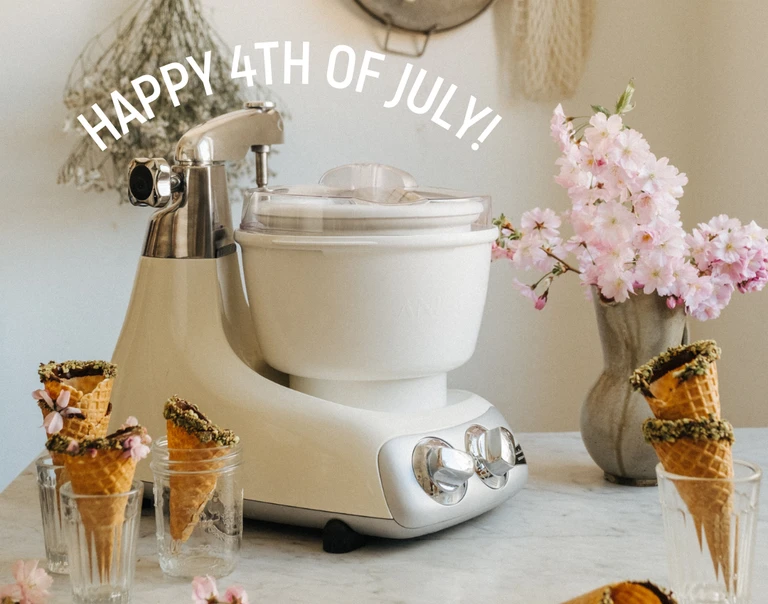 Happy 4th of July! Ankarsrum stand mixer with ice cream bowl attachment, surrounded by waffle cones and pink flowers.