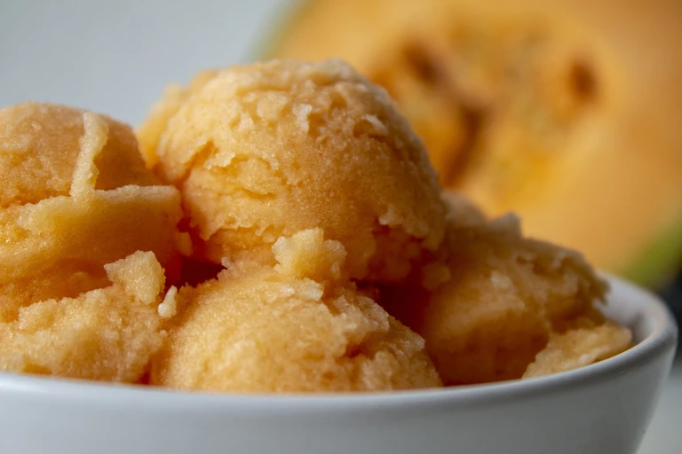 Homemade mango sorbet scoops in a white bowl made with an Ankarsrum stand mixer, fresh mango in background.