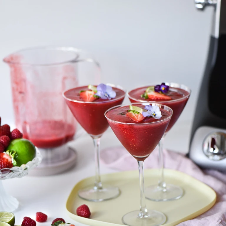 Three elegant strawberry daiquiri cocktails garnished with edible flowers and lime, made with Ankarsrum blender.