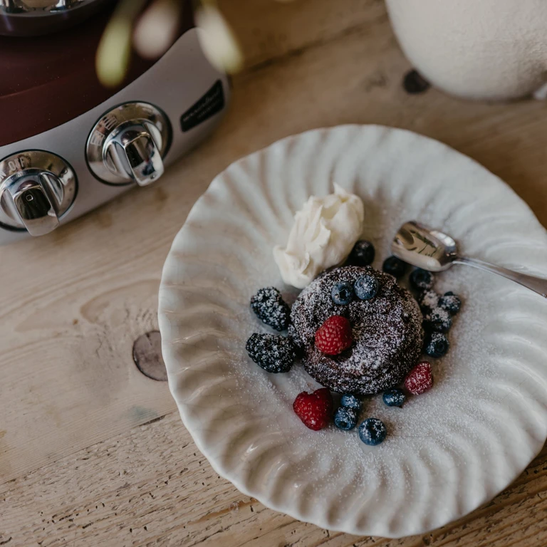 Chocolate lava cake with fresh berries and whipped cream on white plate, beside an Ankarsrum stand mixer.