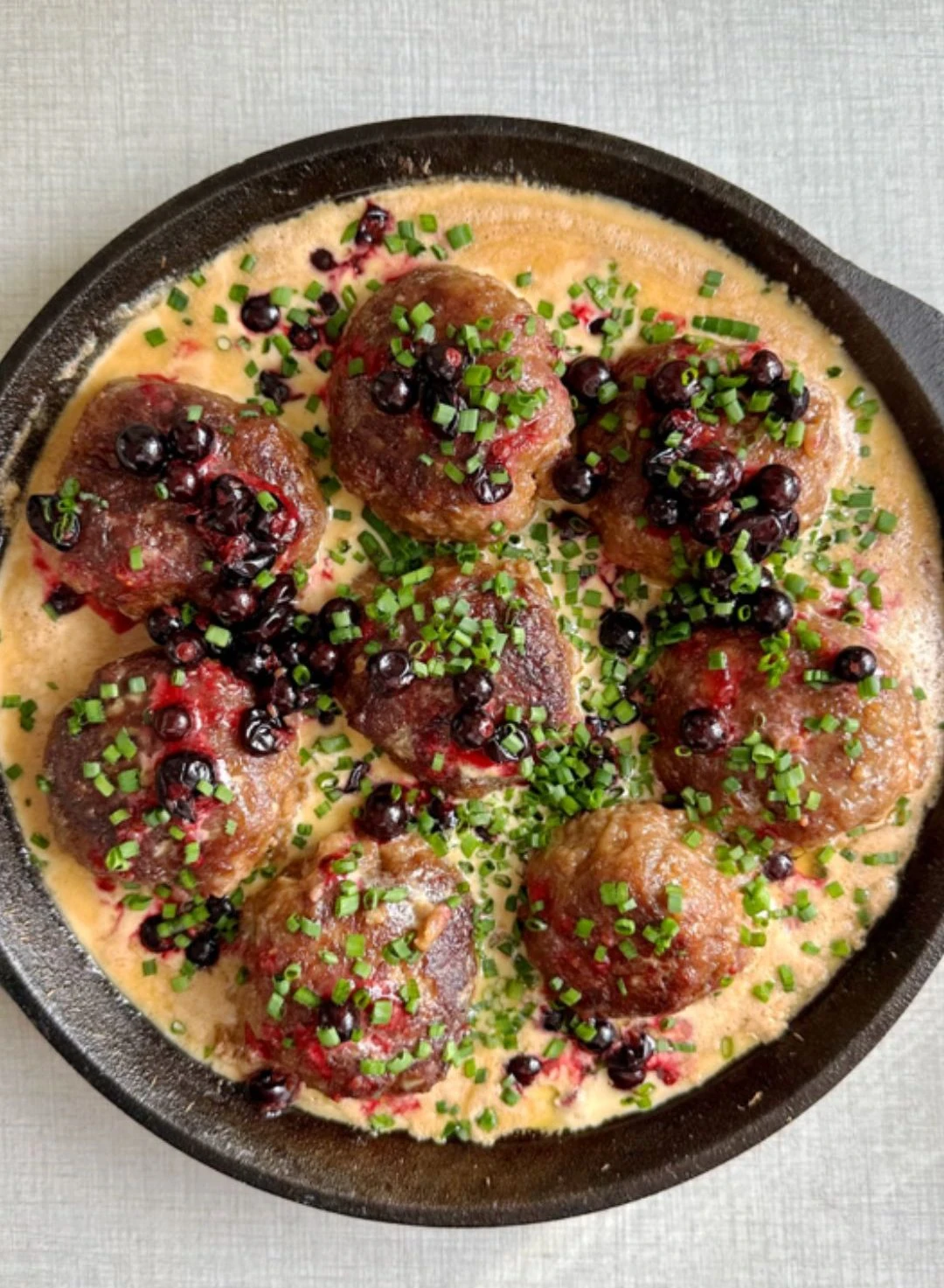 Juicy meatballs with blueberries and chives in creamy sauce, cooked in a cast iron skillet using Ankarsrum stand mixer.