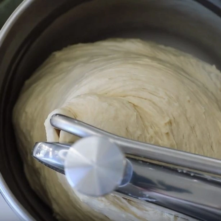 Smooth bread dough being kneaded in an Ankarsrum stand mixer bowl with a dough roller attachment.