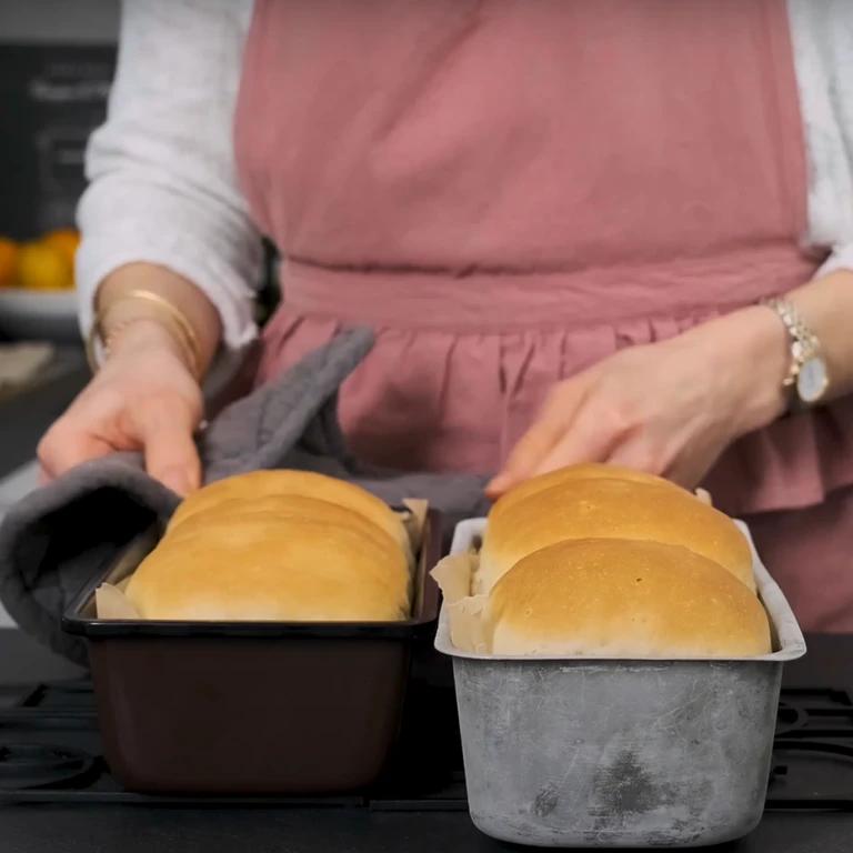 Person in pink apron holding freshly baked bread loaves in dark and silver pans, made with Ankarsrum stand mixer.