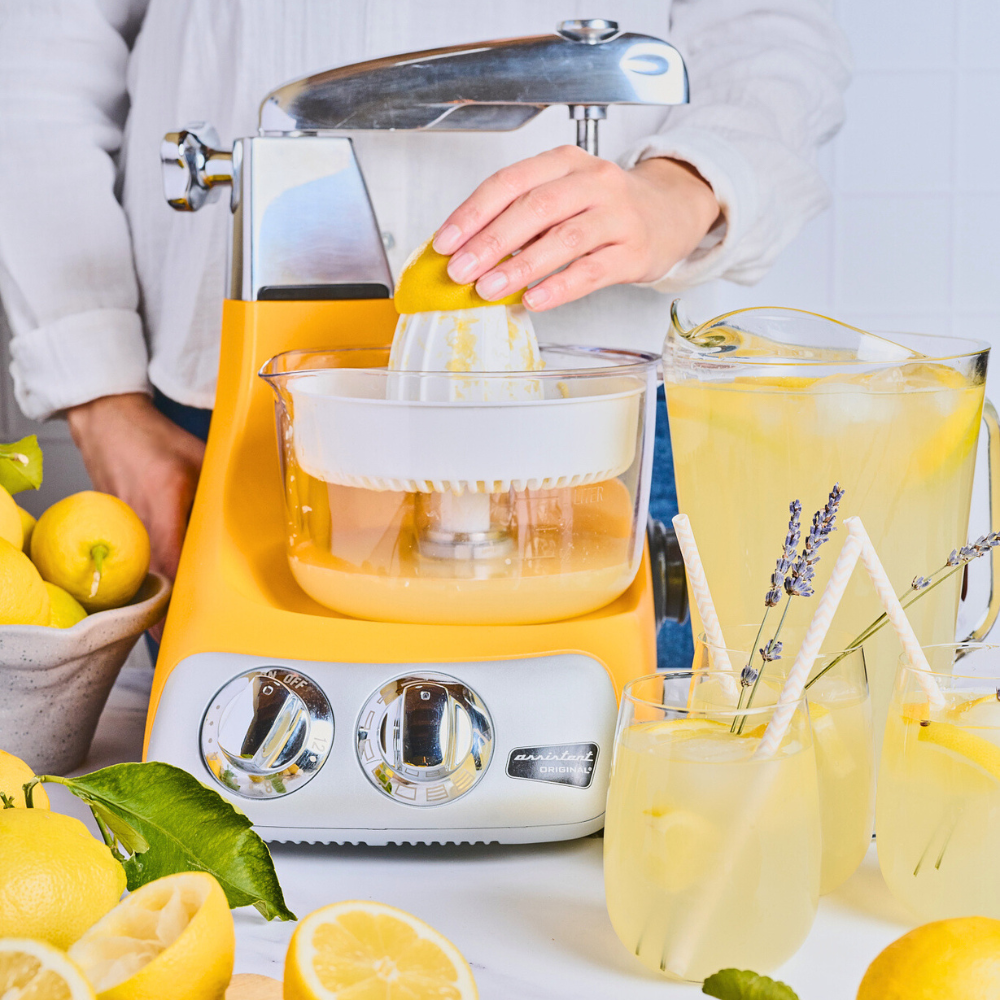 Person som pressar citroner med Ankarsrum köksassistent. Personen har flera citroner och en kanna lemonad vid sidan om maskinen.