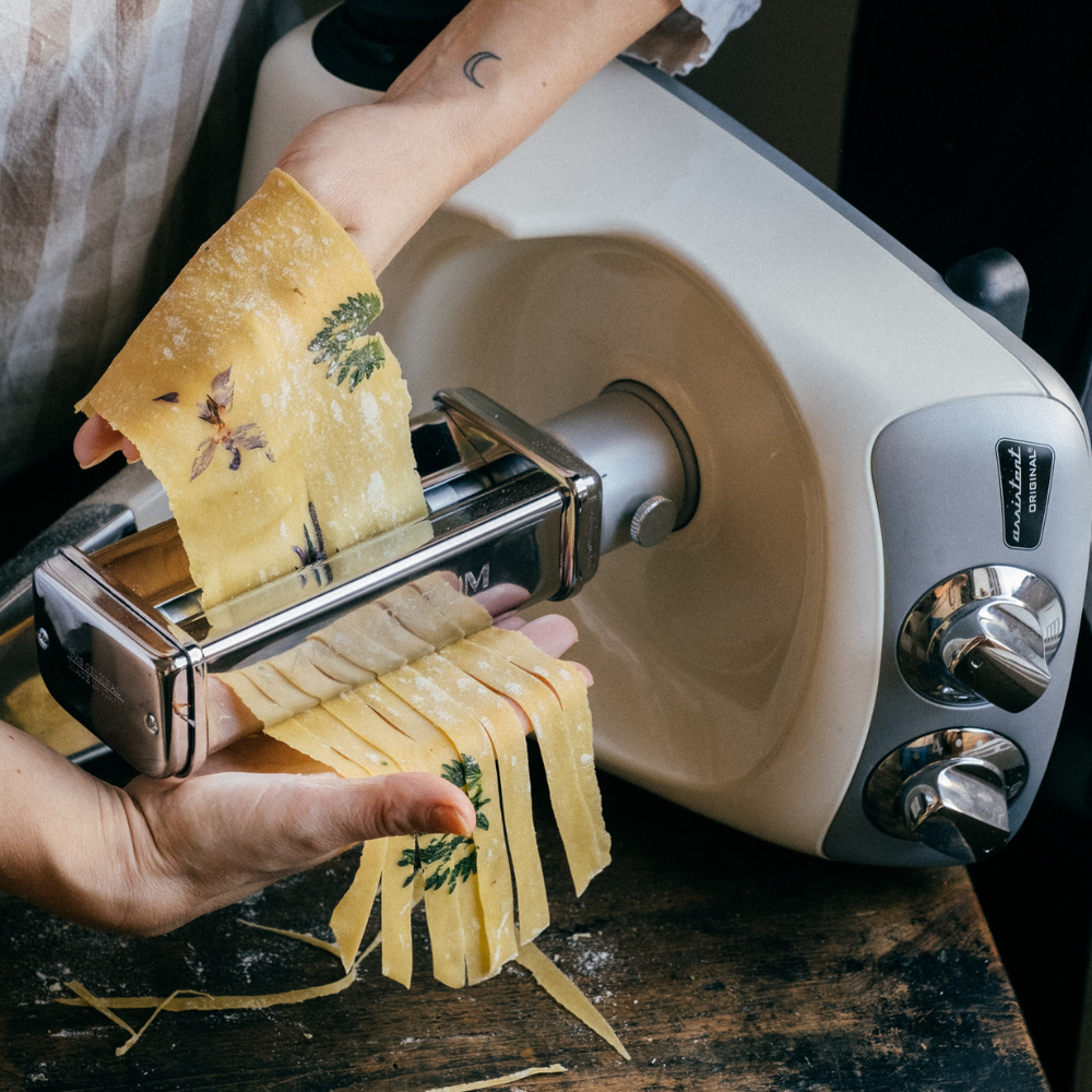 Person som använder Ankarsrums pastavals för fettuccine för att skära pastadeg med inbäddade örter.