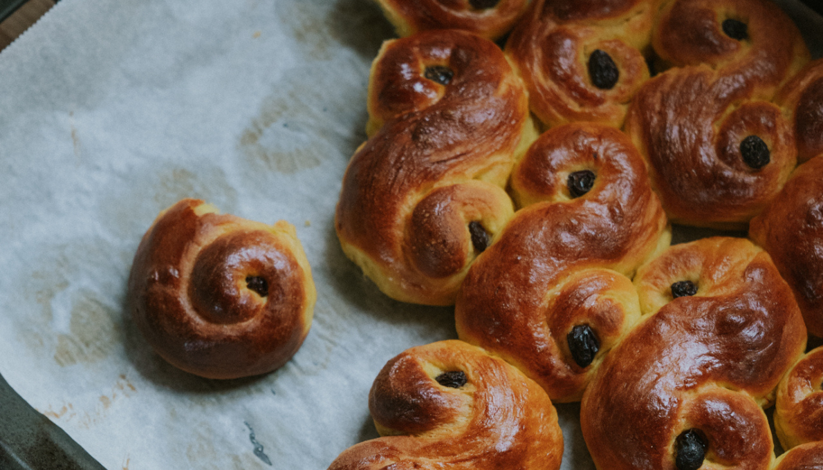 Nygrรคddade lussekatter med russin pรฅ bakplรฅtspapper, en traditionell svensk julbulle.