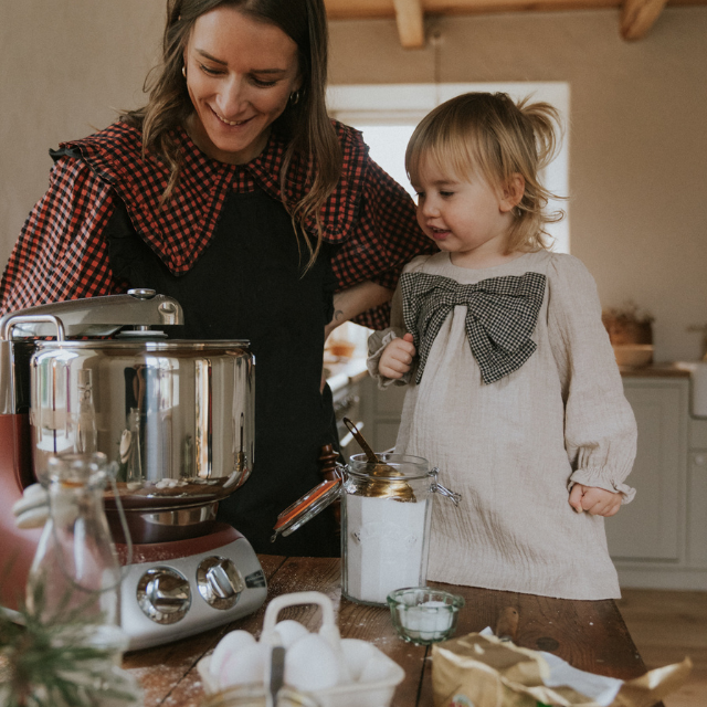 Mamma och barn bakar tillsammans i kรถket med en Ankarsrum Assistent Original kรถksmaskin och ingredienser pรฅ bordet.