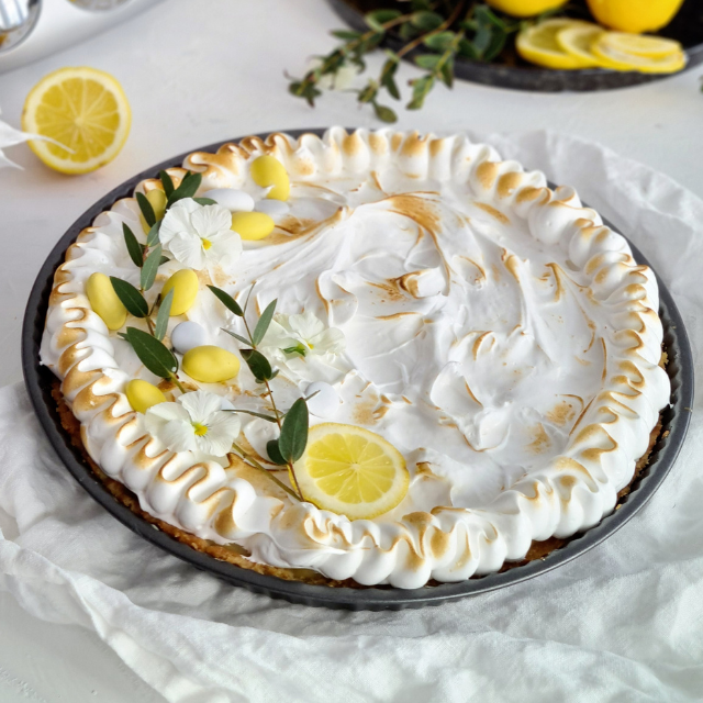 Citronpaj med fluffig maräng, dekorerad med citroner och blommor.