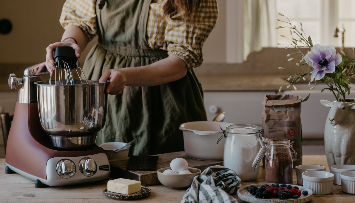 Bakar med Ankarsrum Assistent Original och Vispskål i rostfritt stål på köksbänk med ingredienser.