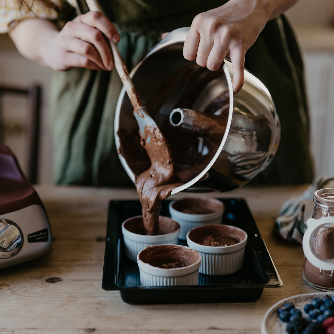 Häller chokladsmet ur Ankarsrum Vispskål i rostfritt stål ner i små formar på en bakplåt.
