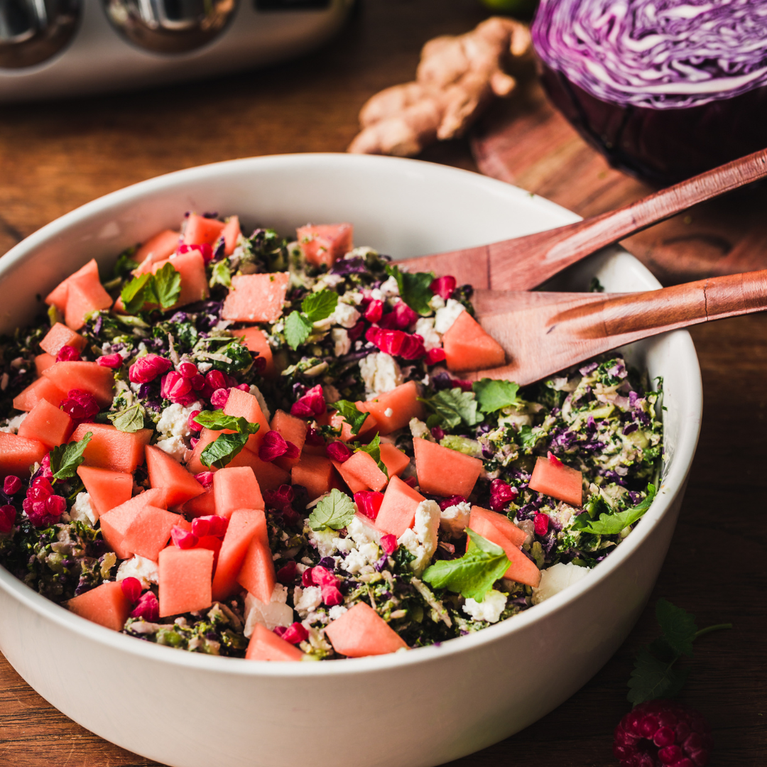 Färgglad sallad med strimlad kål, örter, fetaost, granatäpple och melon i skål.