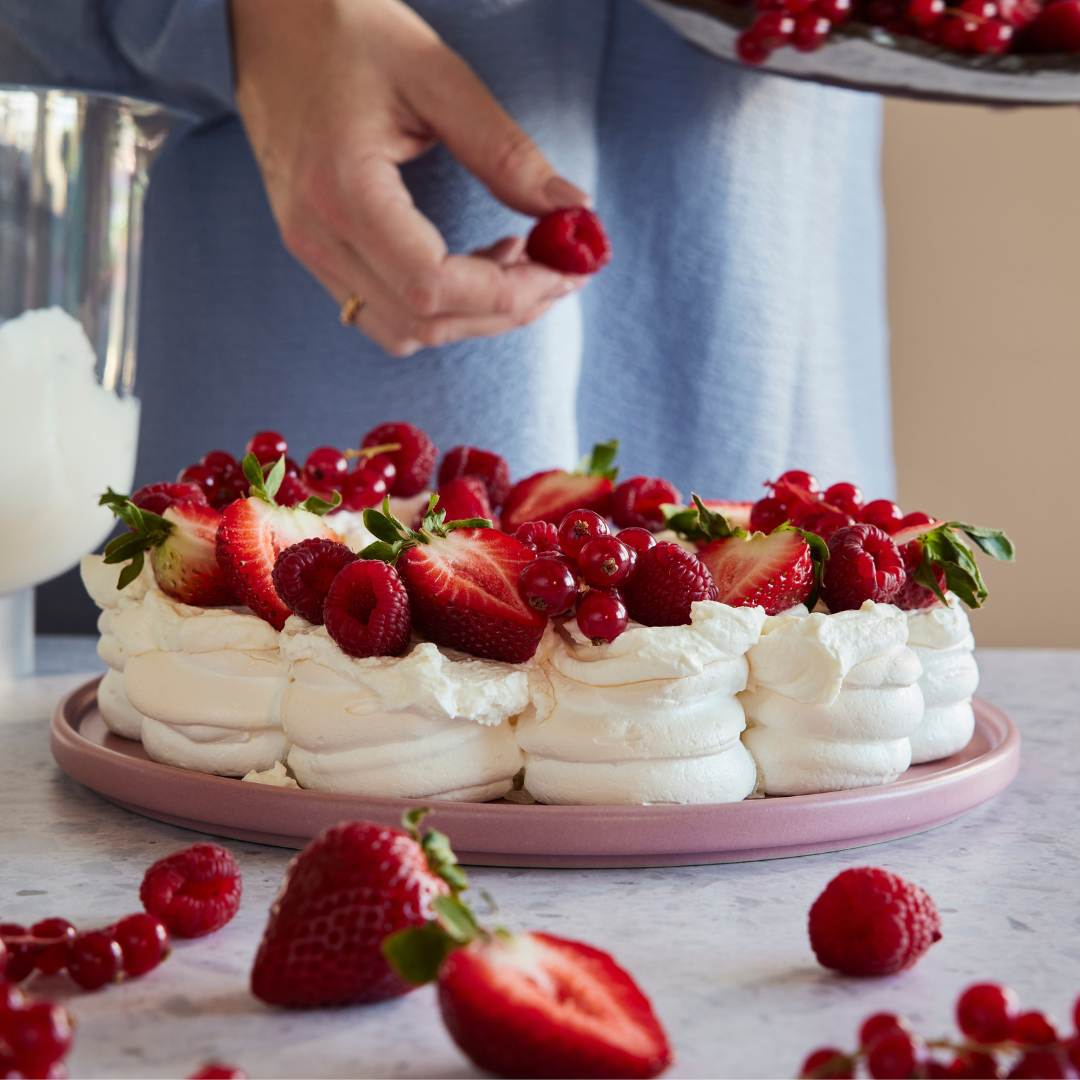 Pavlova toppad med grädde, jordgubbar, hallon och vinbär, serverad till vårens högtider.