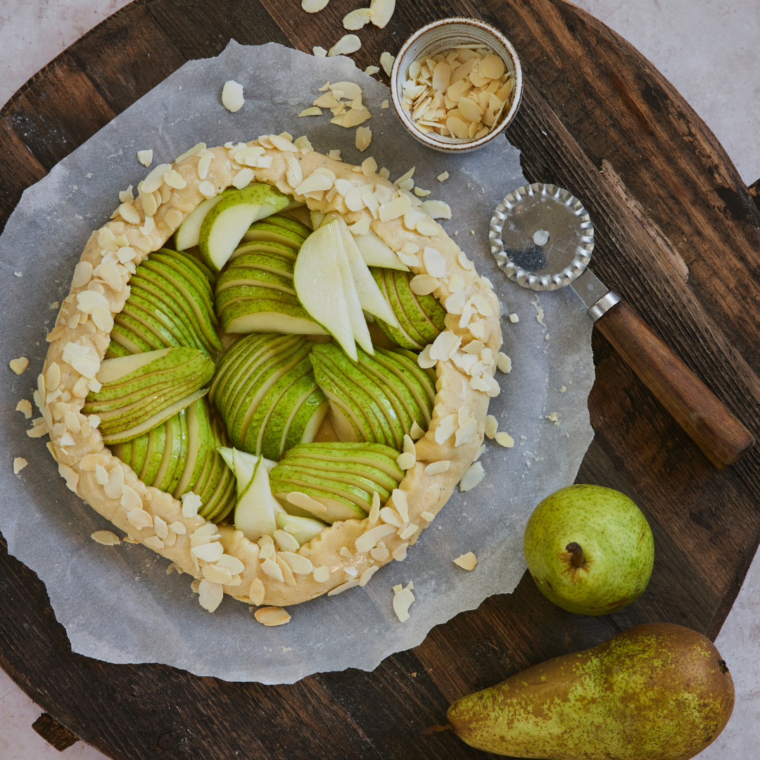 Pärongalette med skivade päron och mandel på rustikt bakbord, perfekt dessert till vårens högtider.
