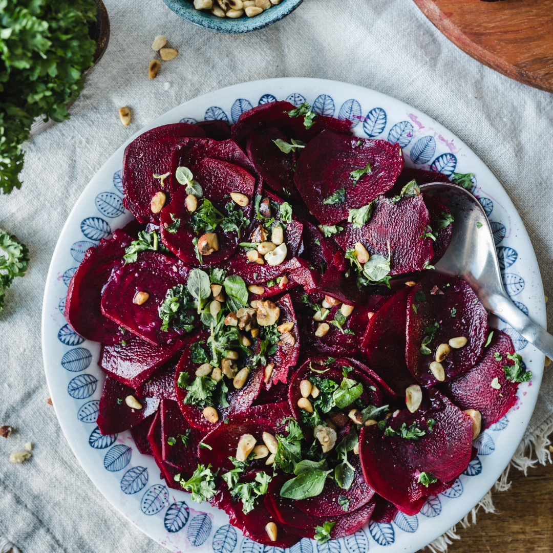 Tunt skivad rödbetscarpaccio med örter och rostade nötter serverad på fat.