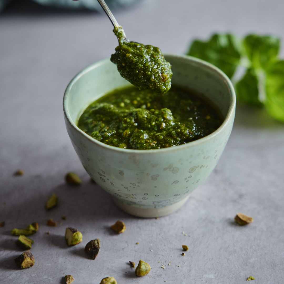 Närbild av en skål med hemgjord pesto toppad med pistagenötter.