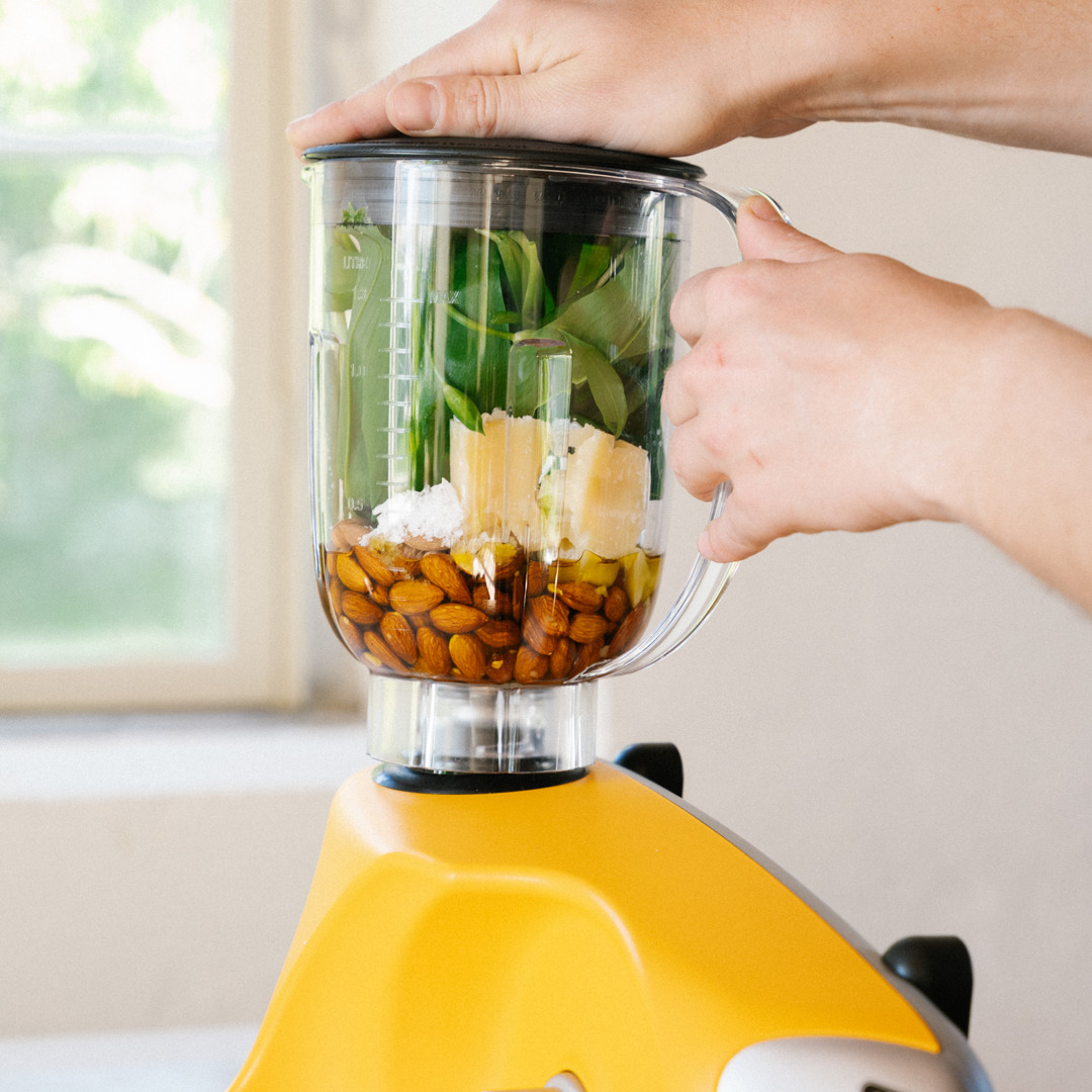 Närbild av Ankarsrums Blender fylld med färska ingredienser som spenat, mandlar, parmesan och olivolja, monterad på en Ankarsrum Assistent Original i Sunbeam Yellow.